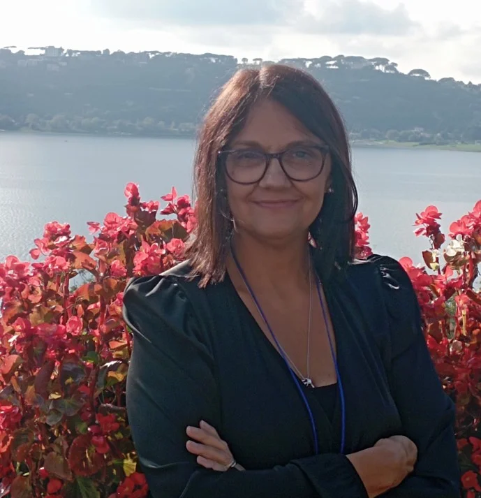 una donna in piedi davanti a un cespuglio fiorito e a uno specchio d'acqua